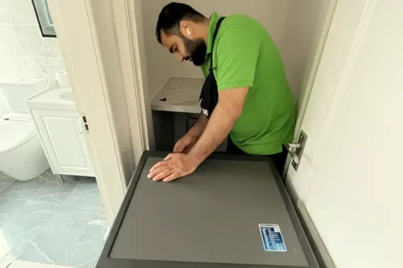 A Mepro Removals expert carefully preparing a Samsung washing machine for moving in a tight Manchester utility space, disconnecting hoses.